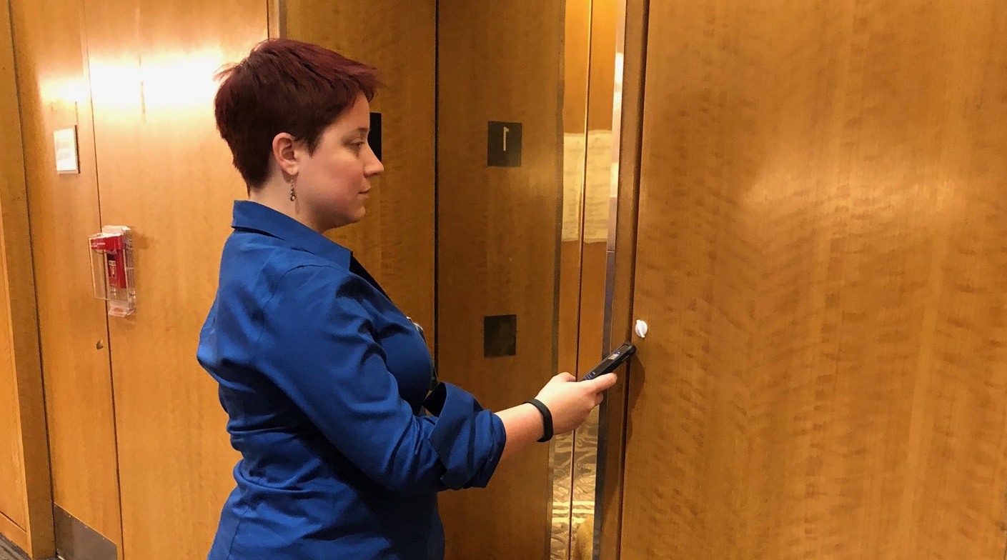 Woman holding phone against a white 3D circular WayTag on the side of an elevator