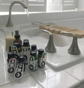 Essential oils with WayClips attached sitting on the edge of a bathtub filled with bubble bath