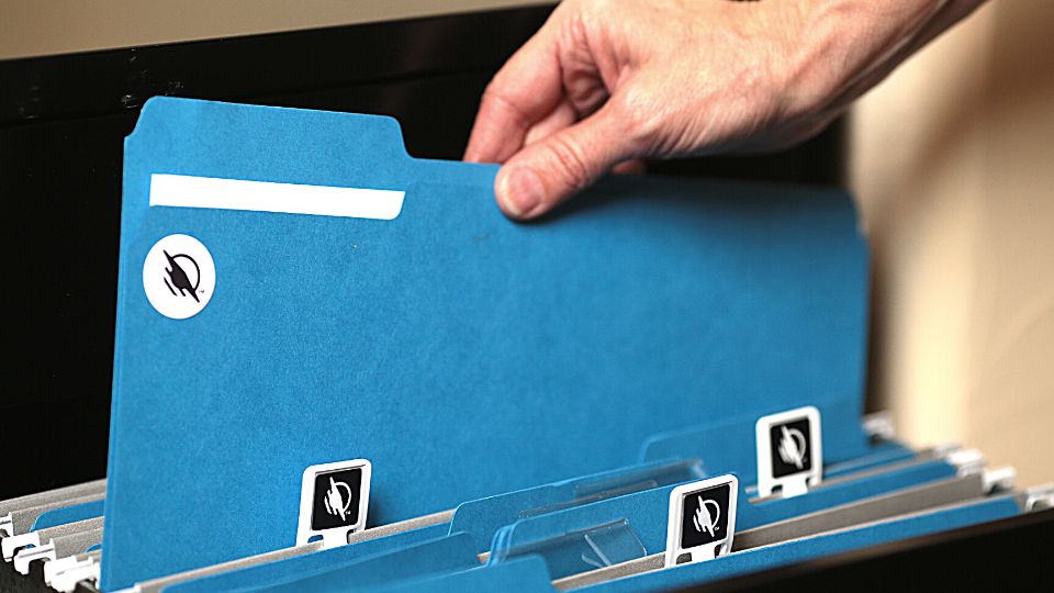 An open file cabinet drawer with blue file folders. Many have WayClips sticking up. A person lifts out one folder with a WayTag sticker on it.
