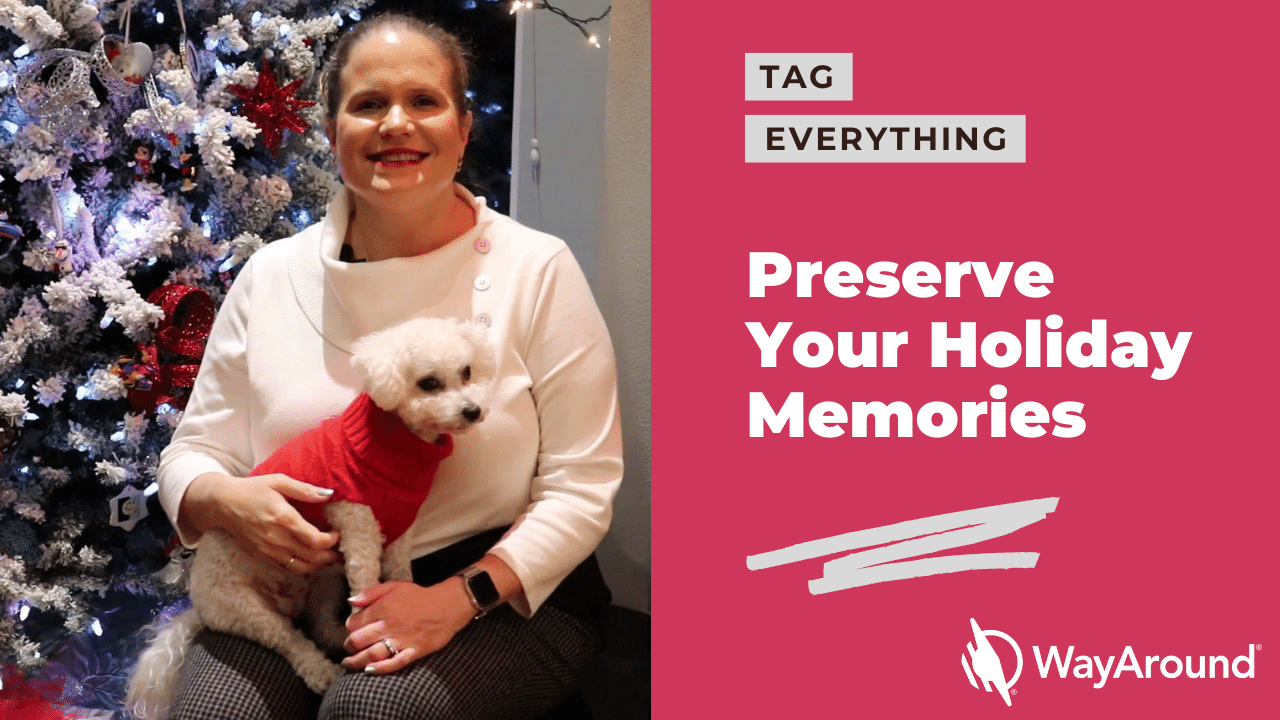 A woman wearing a white sweater is sitting in front of a decorated Christmas. She is holding a small, fluffy dog that is wearing a red sweater. Text says Tag Everything. Preserve Your Holiday Memories.
