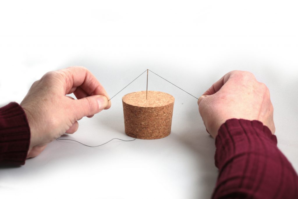 Person threading a self-threading needle inserted into a cork.