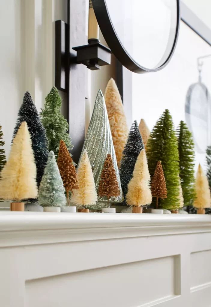 A collection of bottlebrush Christmas trees in green, cream and brown. They are displayed on a mantle with a mirror above.