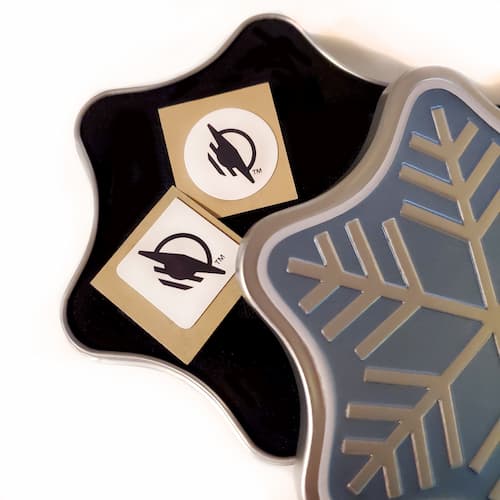 Square and round WayTag stickers sitting inside of a snowflake-shaped black velvet lined box